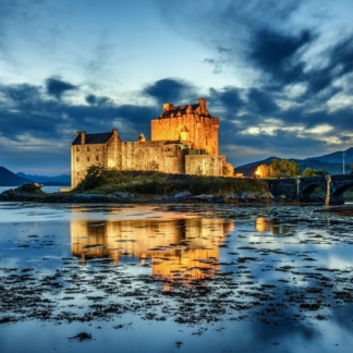 Eilean Donan Castle illuminated during blue hour after sunset, reflecting on calm waters